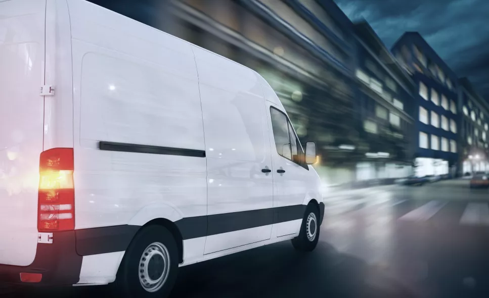 White cargo van driving on a city street at night with motion blur