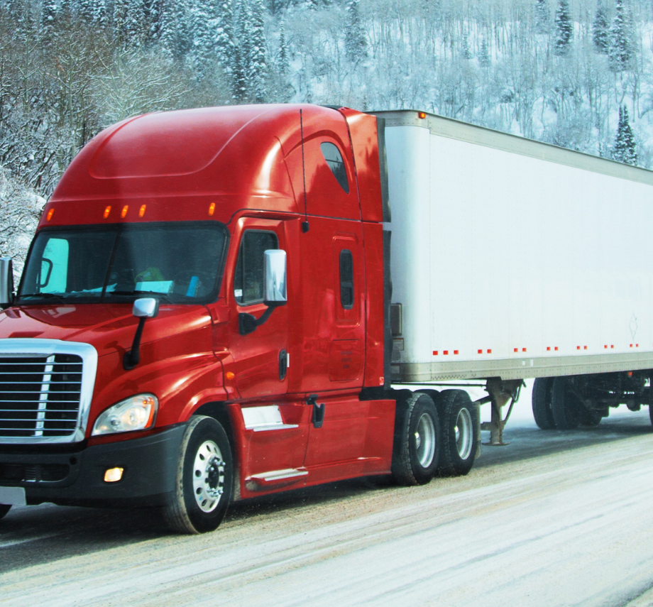 Red semi-truck with a white dry van trailer driving through snowy mountains, showcasing ABS brake monitoring by Road Ready smart trailer telematics solutions