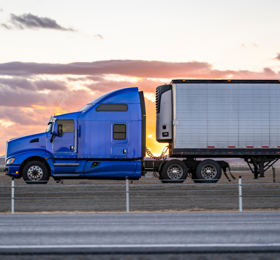 Blue semi-truck hauling a refrigerated trailer at sunset on an open highway