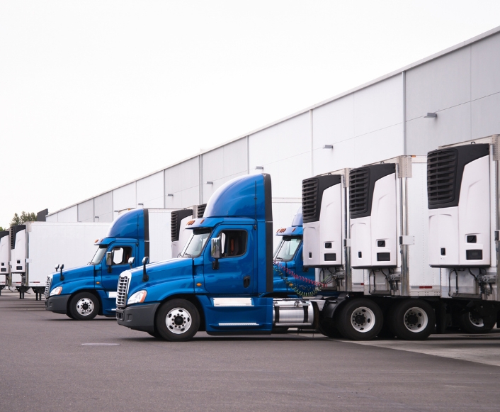 Row of blue semi-trucks with refrigerated trailers at a distribution center